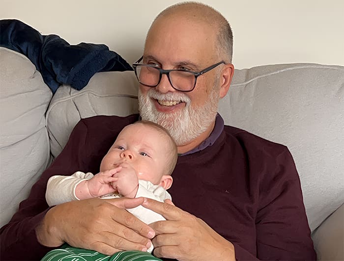 A smiling older man holding a baby on a couch.