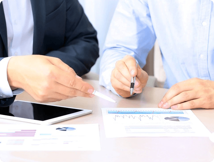Two businessmen sitting at a table with papers and pens.