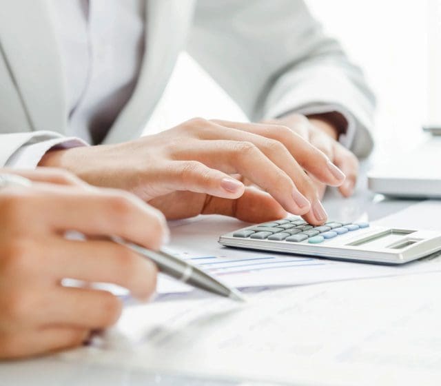 Two people working with a calculator on a desk.