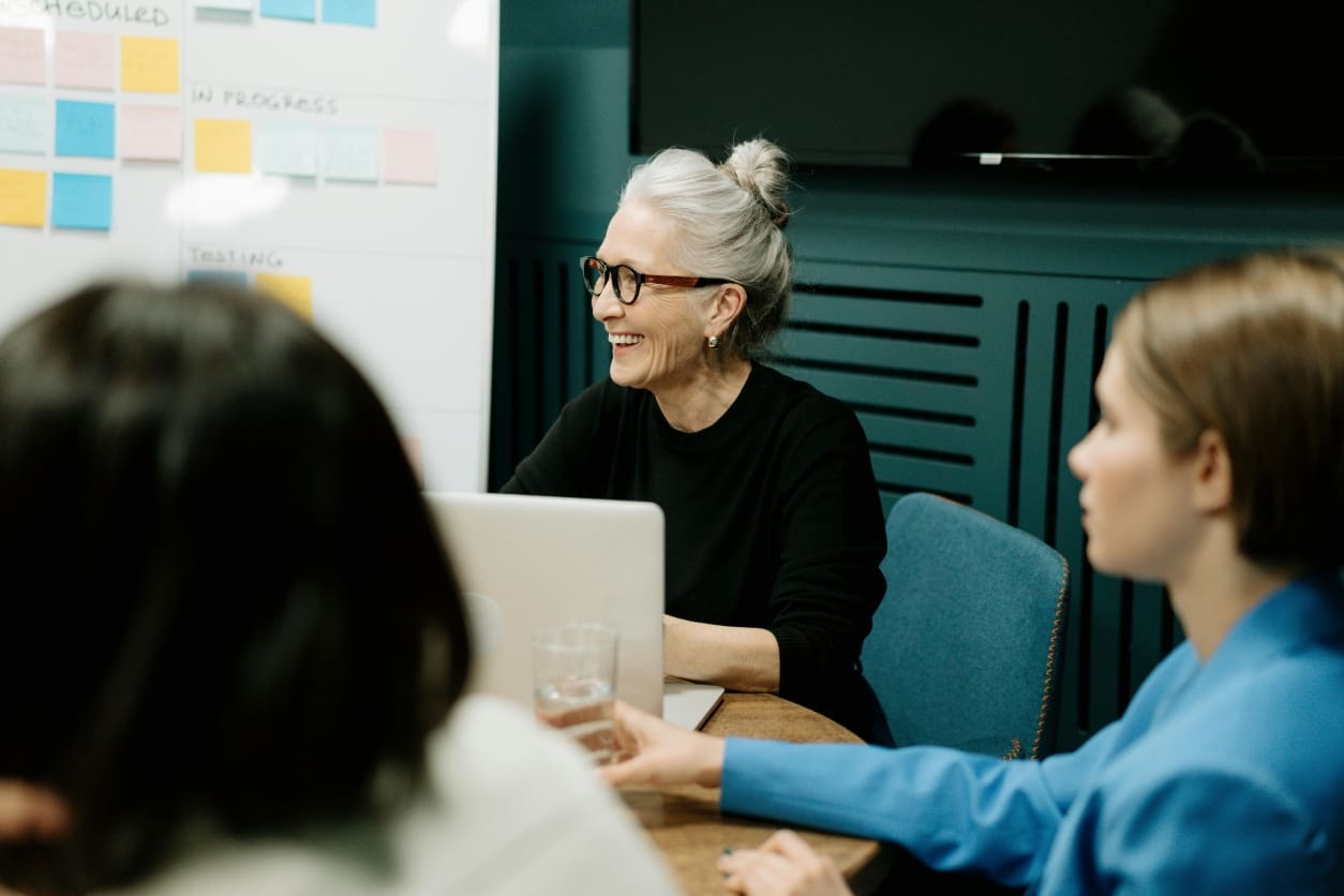 A woman with glasses and gray hair in a bun, smiling during a meeting.