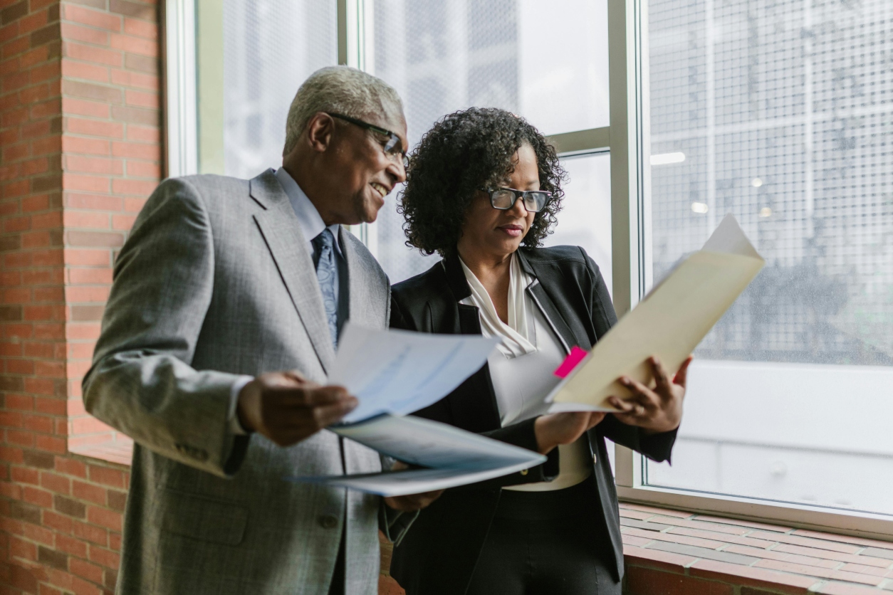 Two professionals reviewing documents in an office with large windows.
