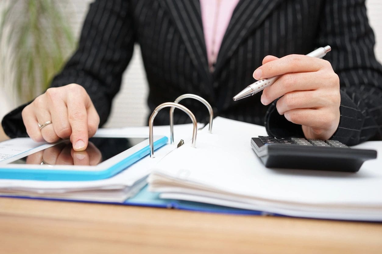 A woman in a business suit is holding a pen and a calculator.